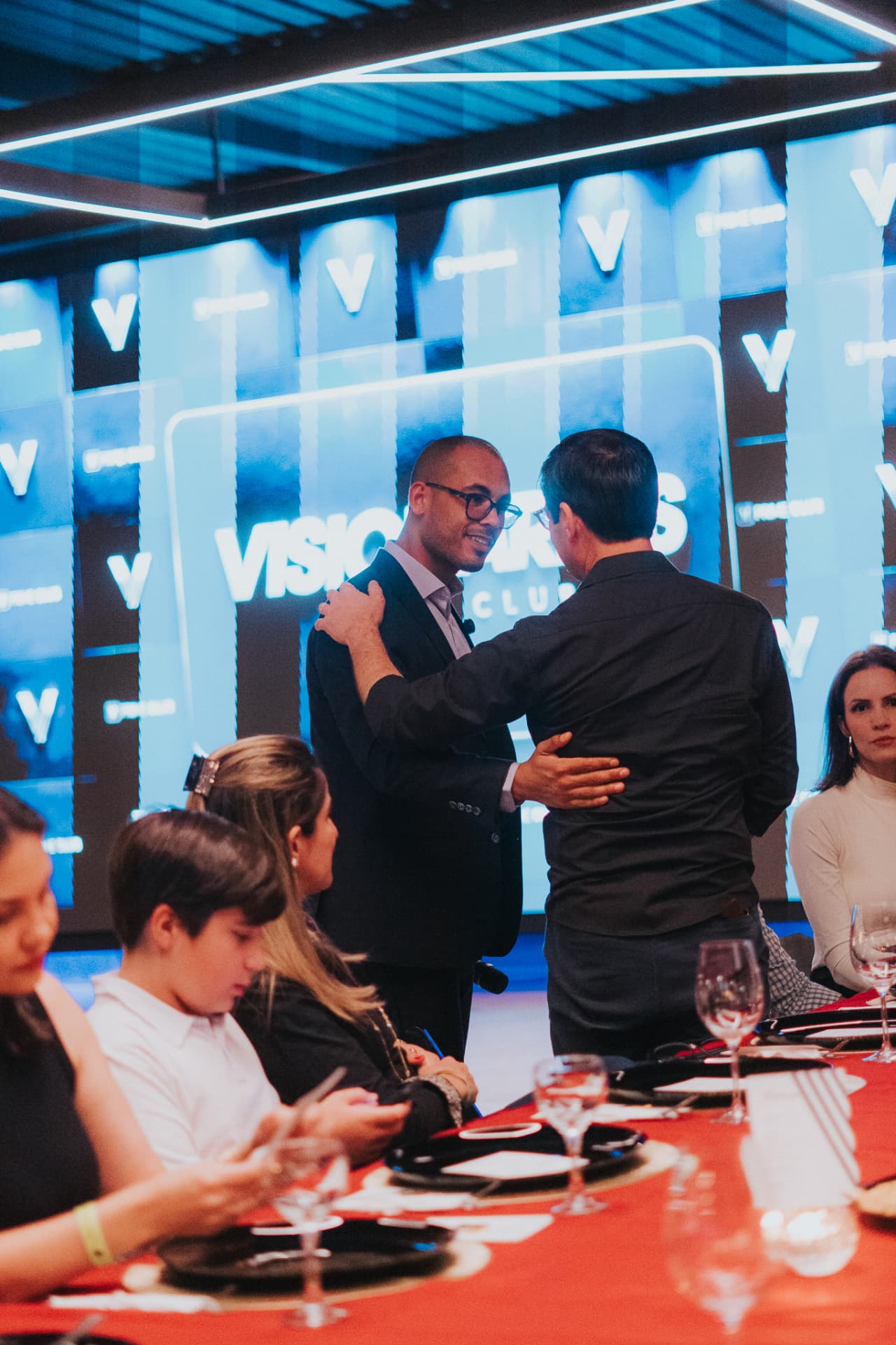 Dois convidados se cumprimentando com um abraço durante um jantar do Prime Club